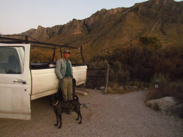 A younger Charlie standing with a dog beside a work truck in the mountains
